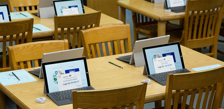 Tablets displaying digitally based assessments on student desks.